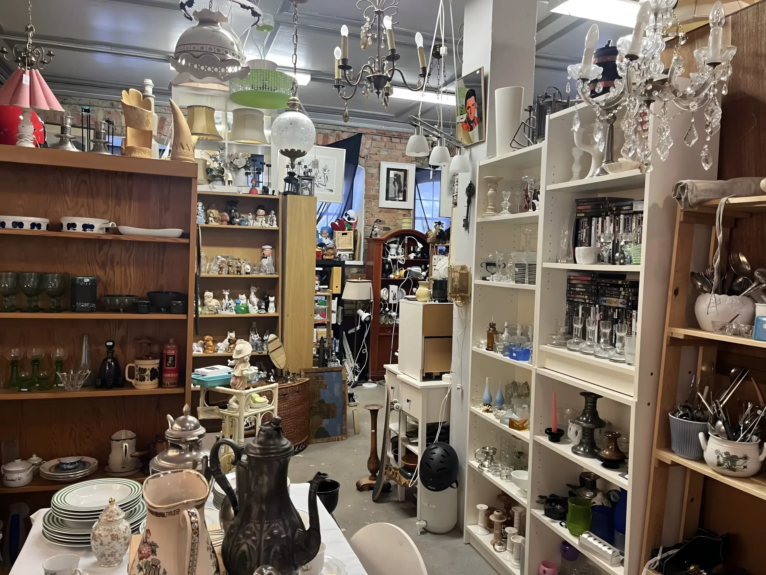 Inne i Gårda Secondhand: hyllor med porslin, glas och inredning samt taklampor och ljuskronor